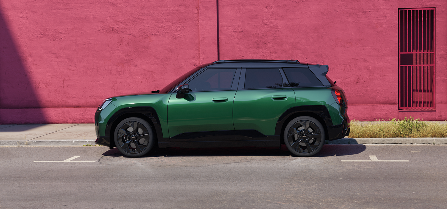 Widok z boku na w pełni elektryczne MINI Aceman w kolorze British Racing Green z czarnym dachem na ulicy.