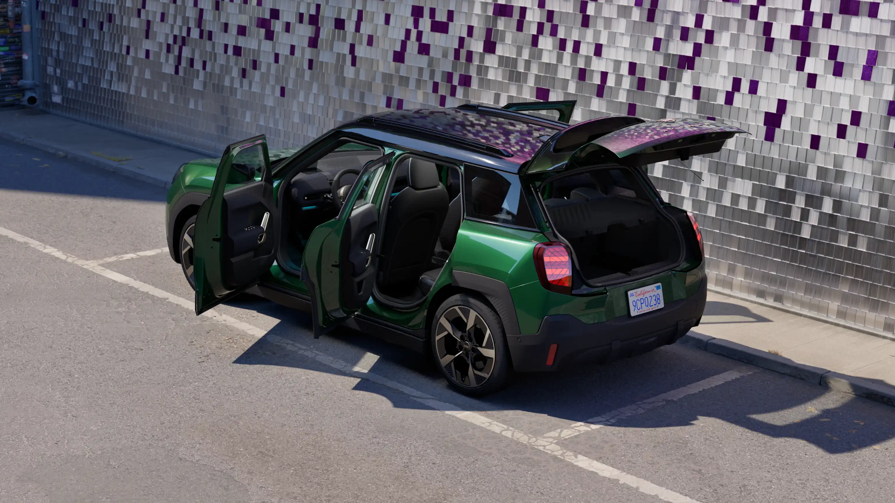 Widok boczny z tyłu zaparkowanego elektrycznego MINI Aceman w kolorze British Racing Green z otwartymi wszystkimi drzwiami i kolorową ścianą w tle