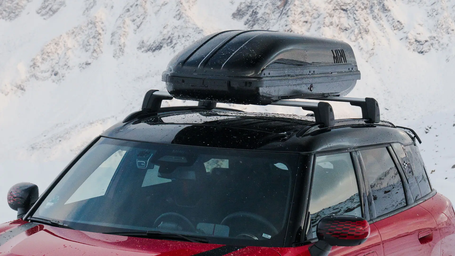 MINI Countryman w kolorze Chili Red II z pojemnikiem dachowym MINI 320 w kolorze czarnym.