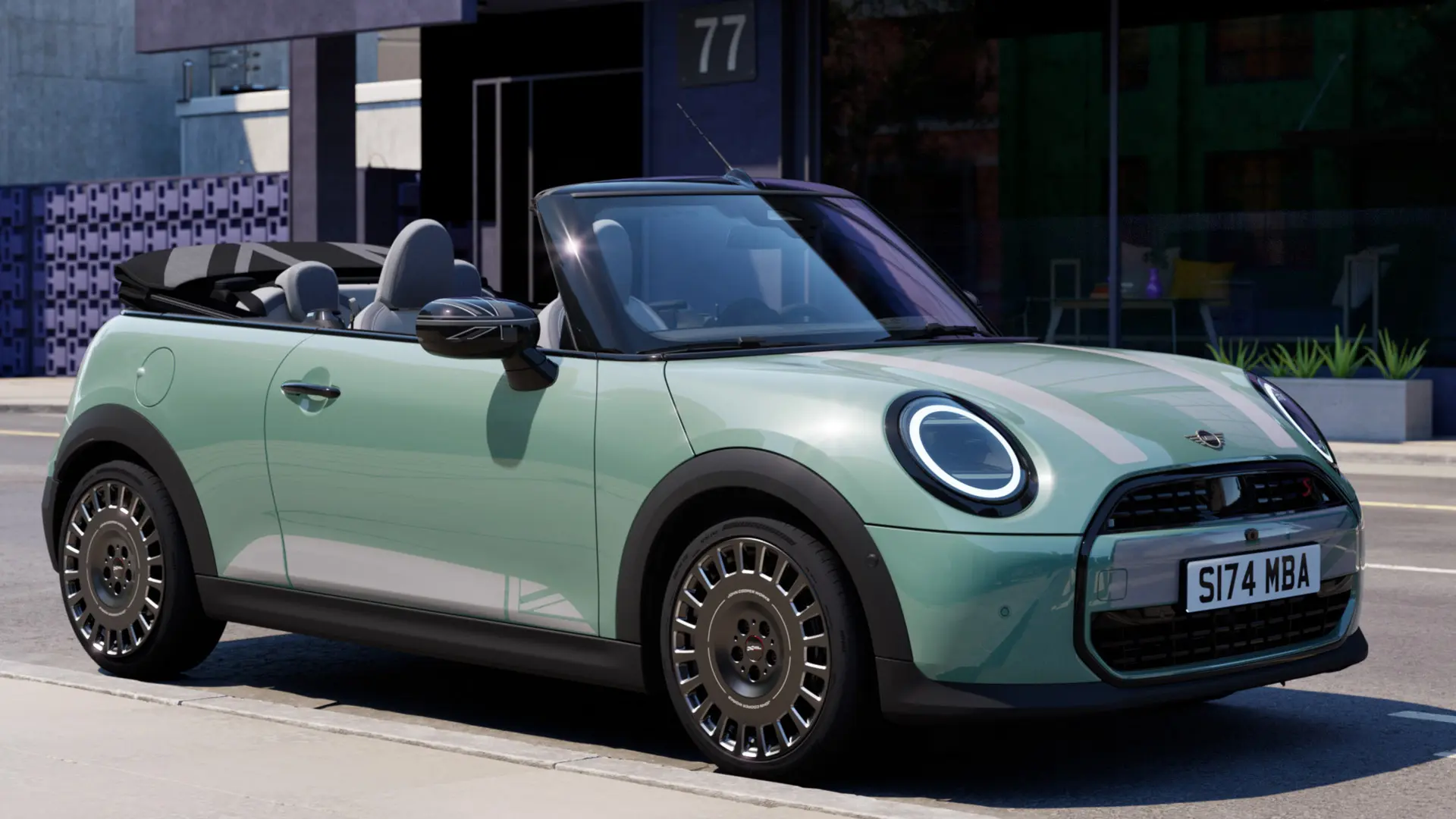Widok z przodu i z boku MINI Cabrio w kolorze Ocean Wave Green z białymi naklejkami MINI Heritage na masce. 