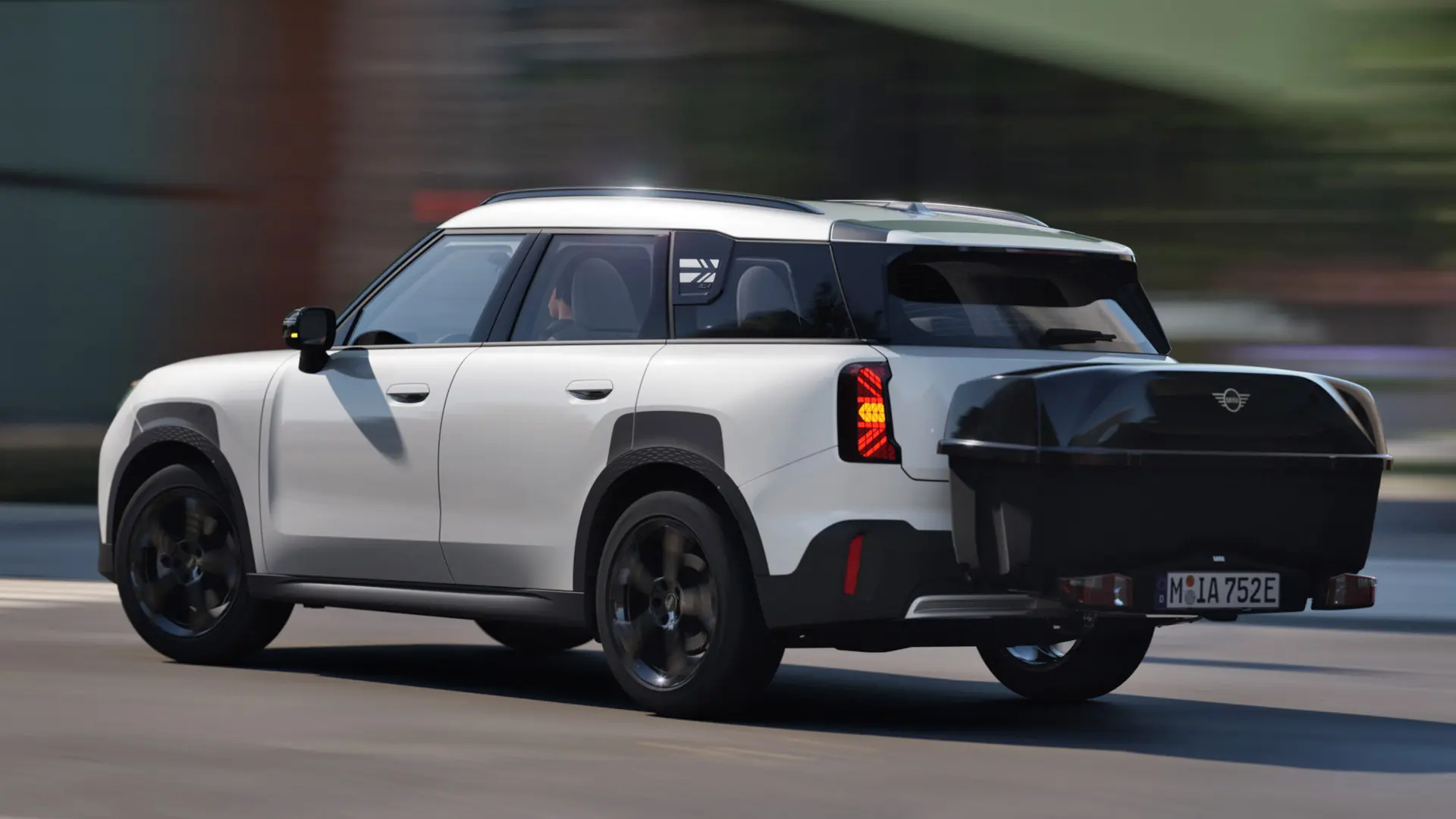 Widok z tyłu i z boku MINI Aceman w kolorze Nanuq White wyposażone w tylny uchwyt rowerowy MINI i przewożące tylną skrzynkę MINI. 