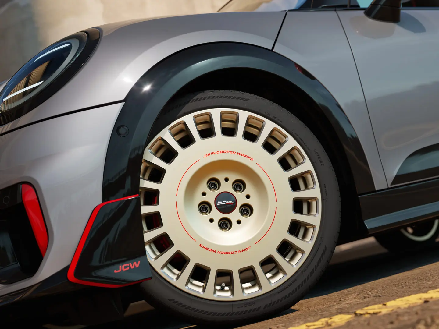 Zbliżenie detali 18-calowej obręczy koła JCW Rallye Spoke 964 w dwukolorowym wykończeniu Vibrant Silver z frezowaniem diamentowym oraz wingletem przednim.