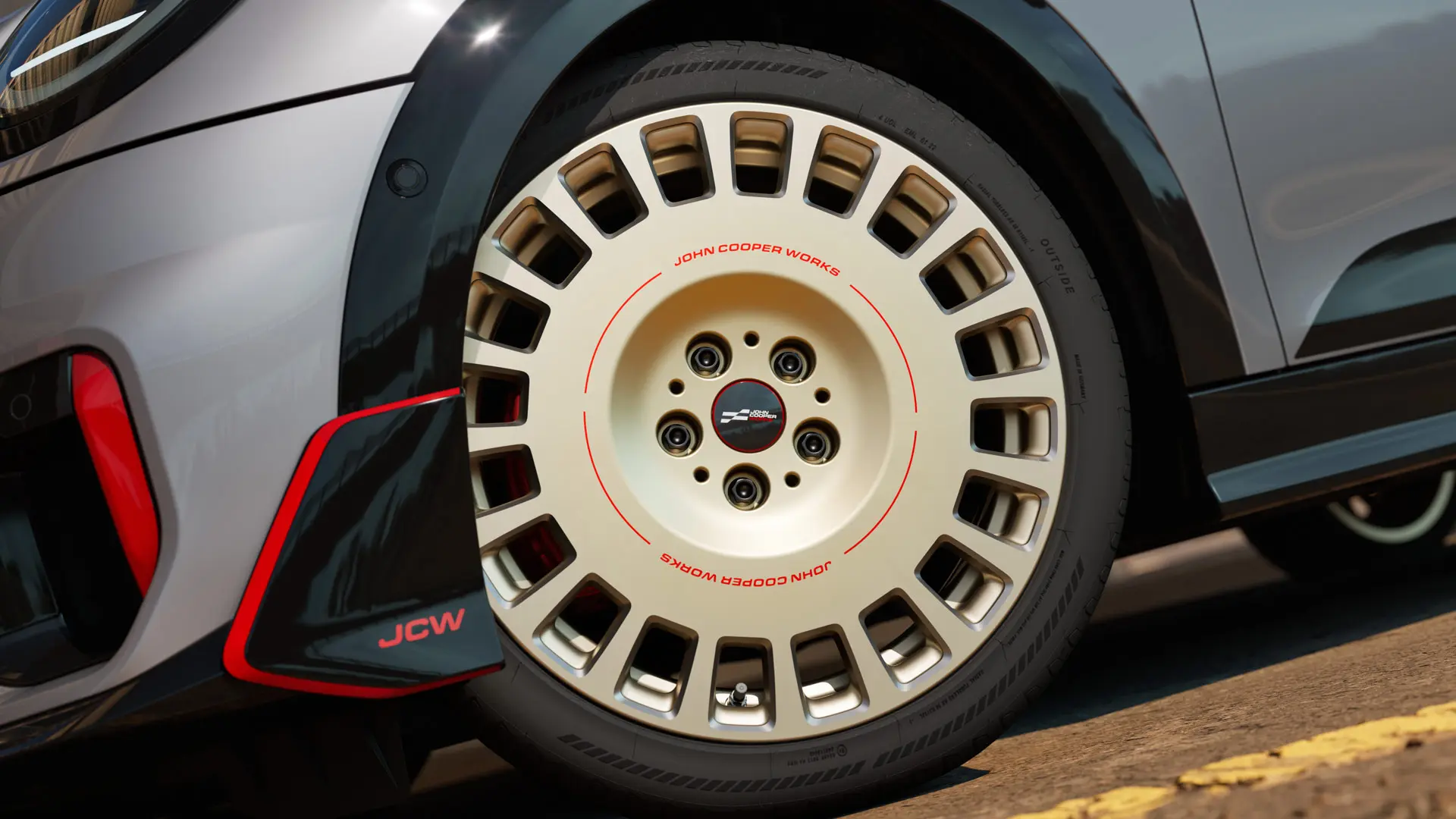 Zbliżenie detali 18-calowej obręczy koła JCW Rallye Spoke 964 w dwukolorowym wykończeniu Vibrant Silver z frezowaniem diamentowym oraz wingletem przednim.