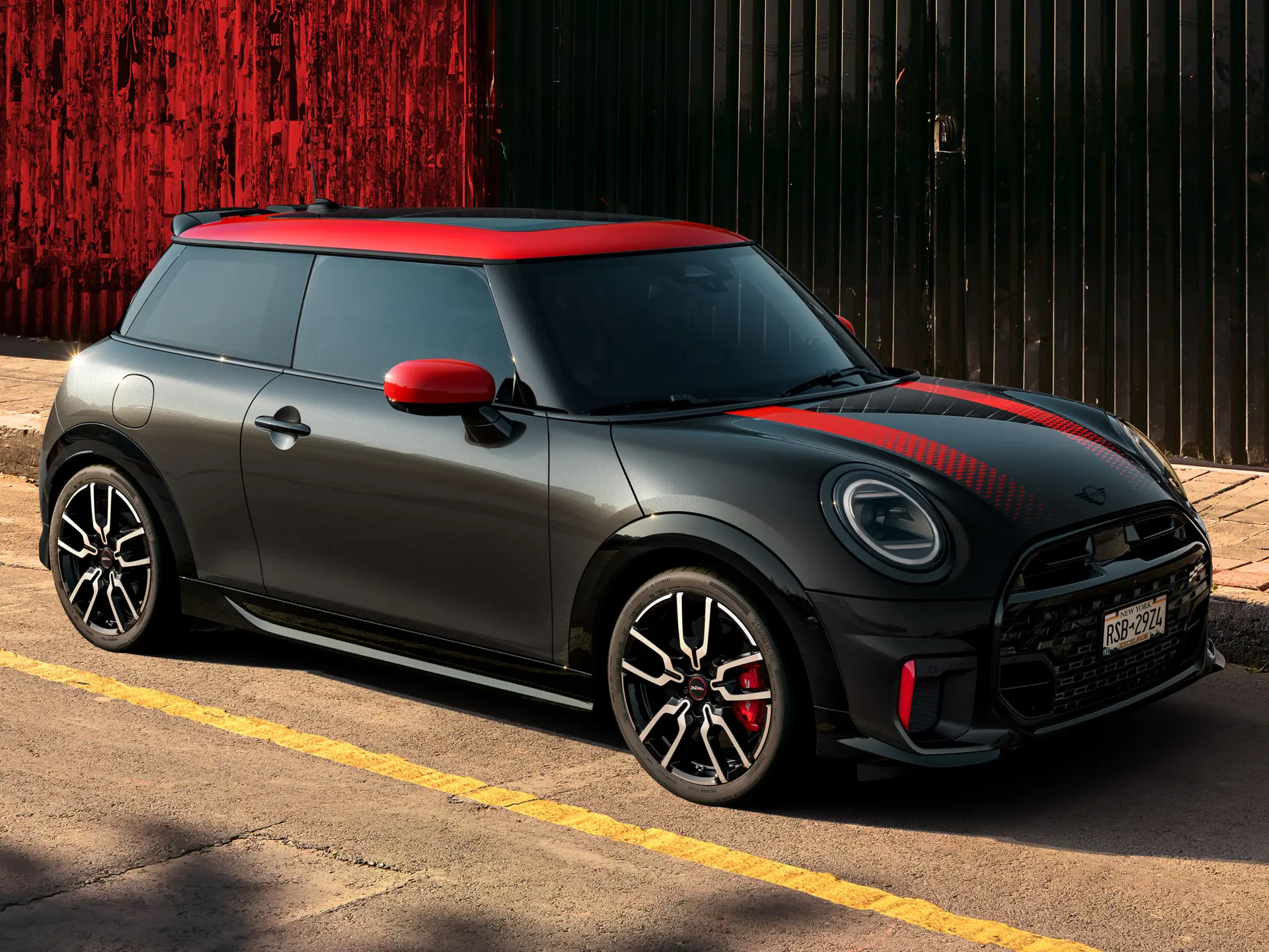 3-drzwiowe MINI John Cooper Works w kolorze Midnight Black z dachem i osłonami lusterek w kolorze Chili Red i czerwonymi paskami sportowymi, widziane z boku i zaparkowane na ulicy.