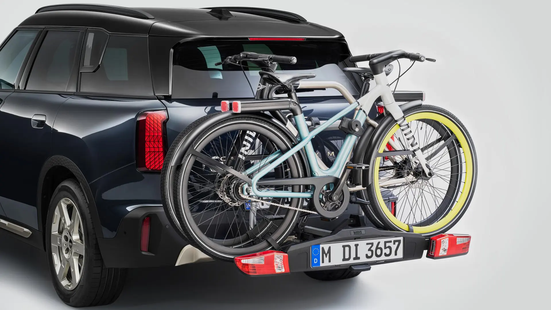 MINI Countryman w kolorze czarnym z bagażnikiem tylnym na rowery i zamontowanymi dwoma rowerami górskimi, widok z tyłu.