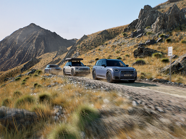 Zdjęcie kilku modeli MINI Countryman Untamed Edition jadących terenową drogą w górach.