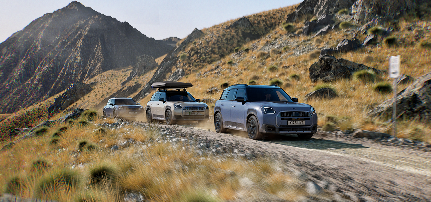 Zdjęcie kilku modeli MINI Countryman Untamed Edition jadących terenową drogą w górach.
