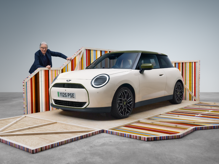 Widok z boku z przodu na w pełni elektryczne MINI Cooper Paul Smith Edition w kolorze Inspired White z projektantem Paulem Smithem