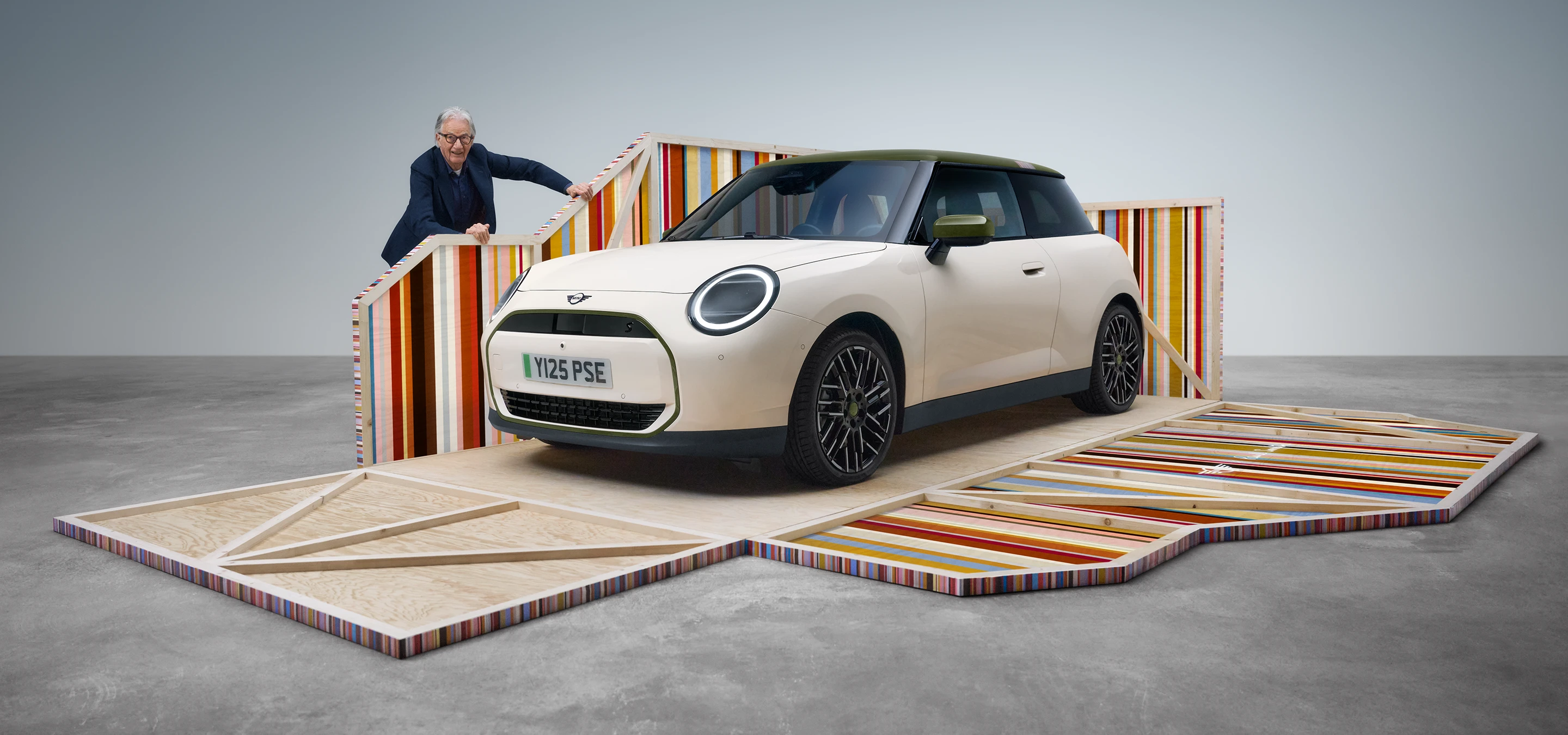 Widok z boku z przodu na w pełni elektryczne MINI Cooper Paul Smith Edition w kolorze Inspired White z projektantem Paulem Smithem