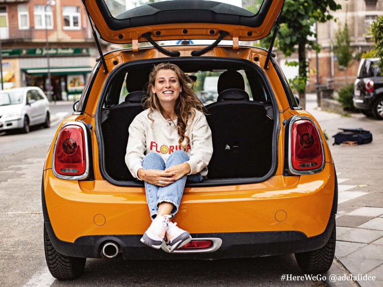 3-drzwiowe MINI Hatch w kolorze Volcanic Orange z uśmiechniętą kobietą siedzącą na krawędzi bagażnika